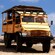 A group of people sit in a safari truck on a dirt road